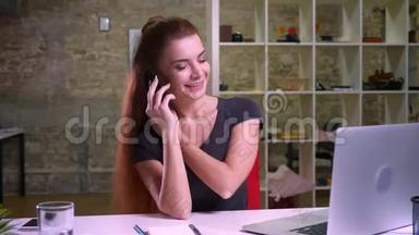 漂亮的红发白种人女人坐着nera手提电脑，一边挂着电话，一边平静地回答